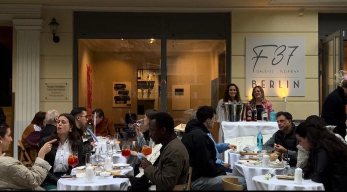 Diverse Gruppe von Gästen sitzt an Tischen in einer Eventlocation mit Getränken und Speisen.