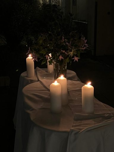 Ein Tisch mit weißen Kerzen und einer Vase mit Blumen in gedämpftem Licht.