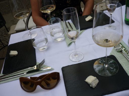 Tischgedeck mit Weingläsern, leeren Gläsern, einem Käsestück und einer Sonnenbrille.