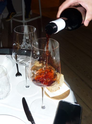 Rotwein wird aus einer Flasche in ein Glas gegossen, mit Brot im Hintergrund.