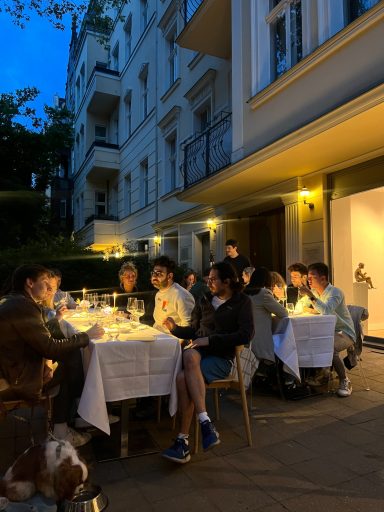 Eine Gruppe von Menschen sitzt abends an einem Tisch im Freien und genießt ein Essen.