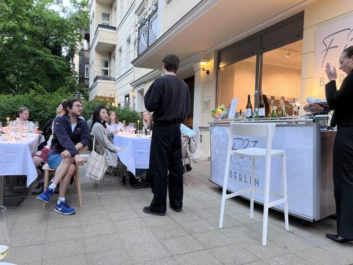 Gartenveranstaltung mit Gästen, Tischen und einem Kellner im Freien.
